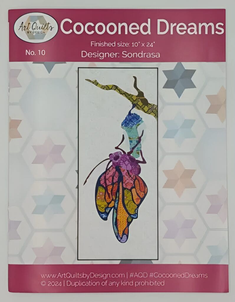 Red Rooster Laser Arts Quilt pattern cover titled Cocooned Dreams by designer Sondrasa. Showcases a colorful butterfly emerging from a cocoon on a branch against a geometric background, with intricate details achieved through laser cutting. Finished size 10 x 24.