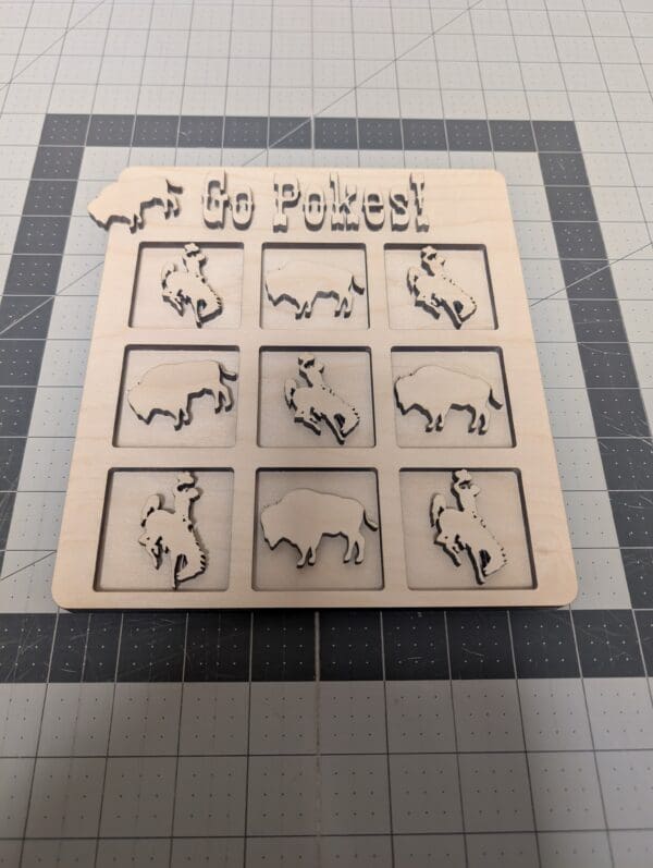 Red Rooster Laser Arts A wooden tic-tac-toe board with Go Pokes! and a Wyoming cutout, featuring bison and bucking horse/rider pieces, rests on a gray mat—perfect to pair with your DIY Small Wooden Steamboat Home Sign kit.