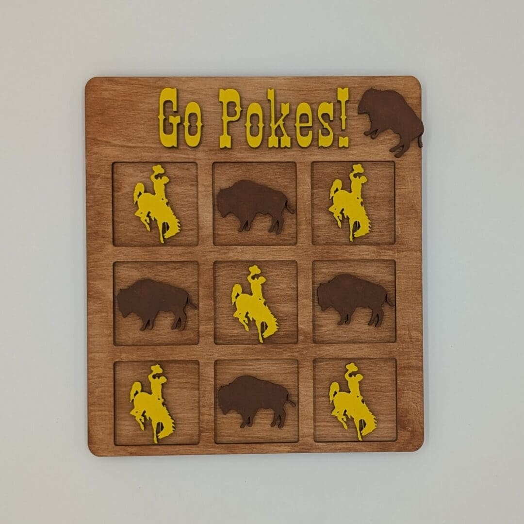 Red Rooster Laser Arts A wooden tic-tac-toe board with buffalo and cowboy rider pieces. “Go Pokes!” in yellow tops the board with a buffalo graphic—perfect to pair with your DIY Small Wooden Steamboat Home Sign.