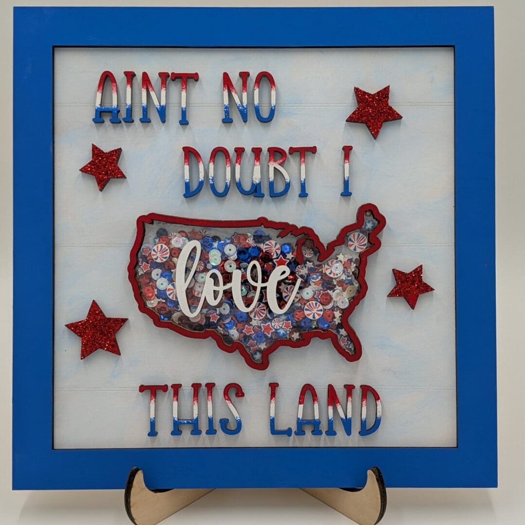 Red Rooster Laser Arts The DIY Patriotic Shaker Sign Kit - Love This Land includes a blue-bordered frame with “Aint No Doubt I Love This Land” around a USA map, red, white, and blue accents, four glittery red stars, and a wooden easel for display. Red Rooster Laser Arts The DIY Patriotic Shaker Sign Kit - Love This Land includes a blue-bordered frame with “Aint No Doubt I Love This Land” around a USA map, red, white, and blue accents, four glittery red stars, and a wooden easel for display.