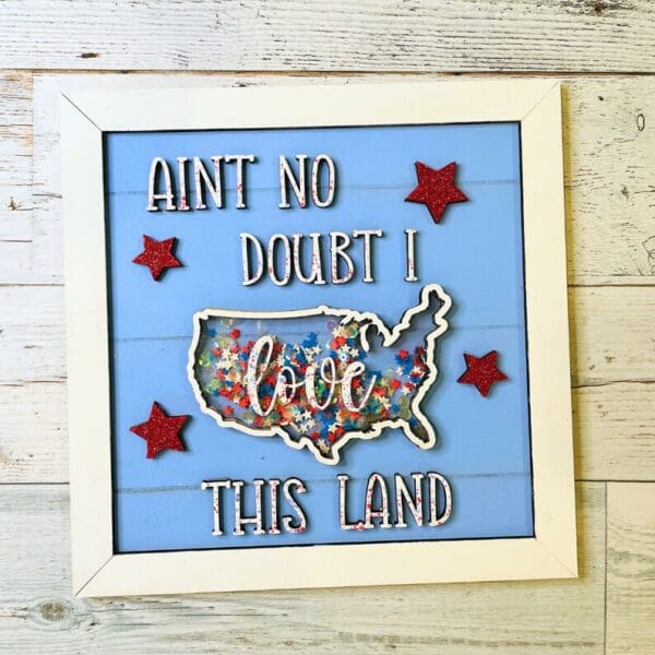 Red Rooster Laser Arts The DIY Patriotic Shaker Sign Kit - Love This Land features a blue background, four red glitter stars, white AINT NO DOUBT I love THIS LAND text, and a confetti-filled U.S. map—perfect for festive celebrations!.