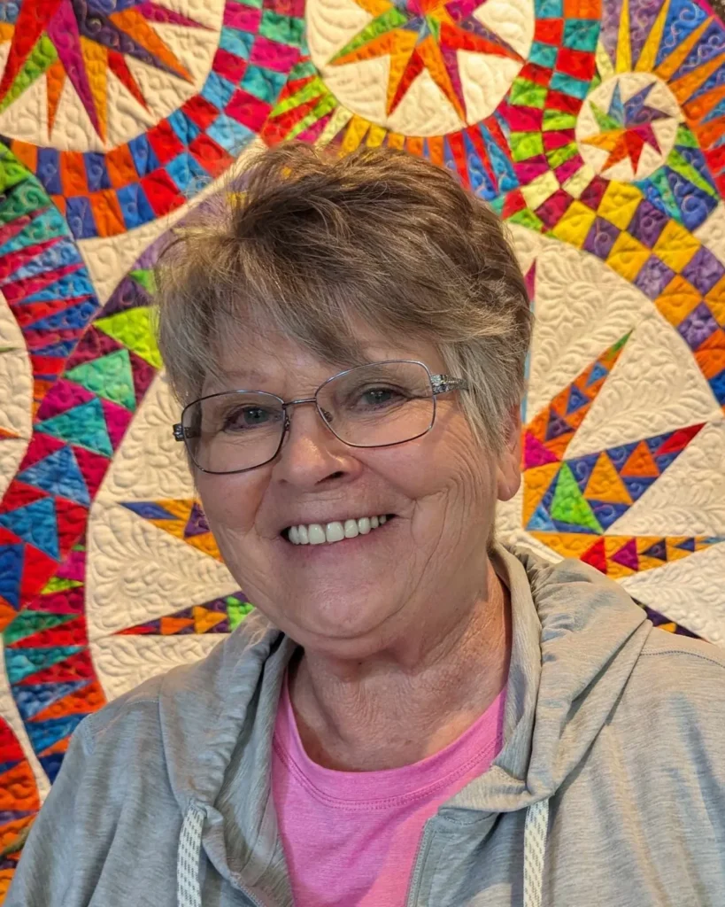 A woman standing in front of a quilt.