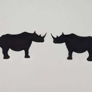 Red Rooster Laser Arts Two laser-cut rhinoceros silhouettes from the Set of 2 Rhinoceros, Laser Cut, Pre-Fused face each other on a white background. Their solid black shapes emphasize their distinct horns and sturdy bodies in an artistic blend of nature and craftsmanship. These are laser cut and pre fused appliques, made from high quality quilting cotton.