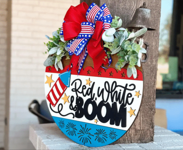 Red Rooster Laser Arts The DIY Door Hanger Kit - Red, White and BOOM! features a heart-shaped design with greenery, a patriotic bow, stars, fireworks, and Red, White & BOOM text—perfect for festive Fourth of July decor.