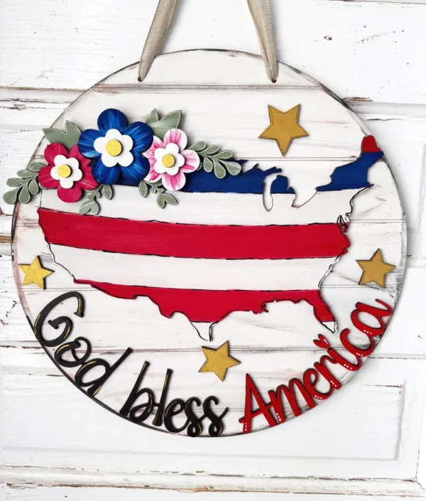 Red Rooster Laser Arts The DIY Door Hanger Kit - God Bless America is a charming round wooden sign with a U.S. map, red, white, and blue stripes, flowers, stars, and God bless America in black and red—perfect for patriotic decor!.
