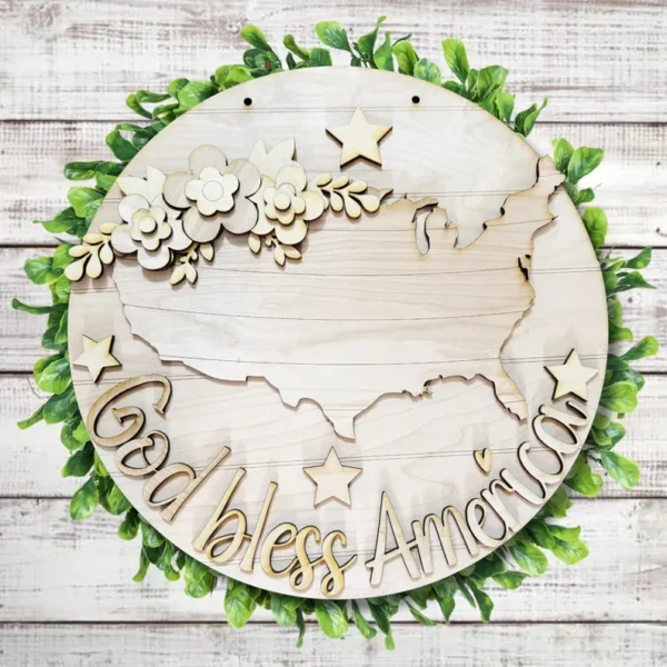 Red Rooster Laser Arts The DIY Door Hanger Kit - God Bless America includes a round wooden sign with a cutout USA map, greenery, floral accents, stars, and “God Bless America” script on whitewashed wood planks—perfect for customizing your door.