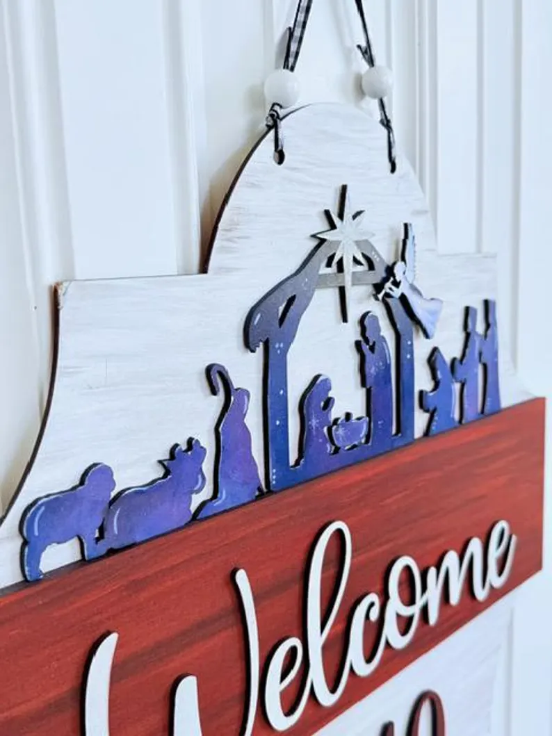Red Rooster Laser Arts The Interchangeable Door Hanger Insert - Nativity Scene is a DIY kit featuring a wooden sign with a blue and white nativity silhouette, “Welcome” in white script, and Mary, Joseph, baby Jesus, animals, and a star.