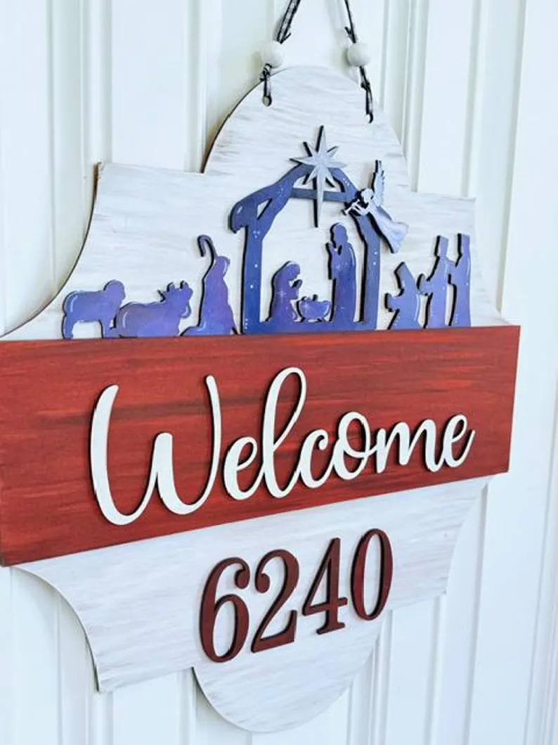 Red Rooster Laser Arts The Interchangeable Door Hanger Insert - Nativity Scene DIY kit features a nativity scene silhouette above “Welcome” in script and house number 6240, set on a white and red background for Christmas Eve décor.