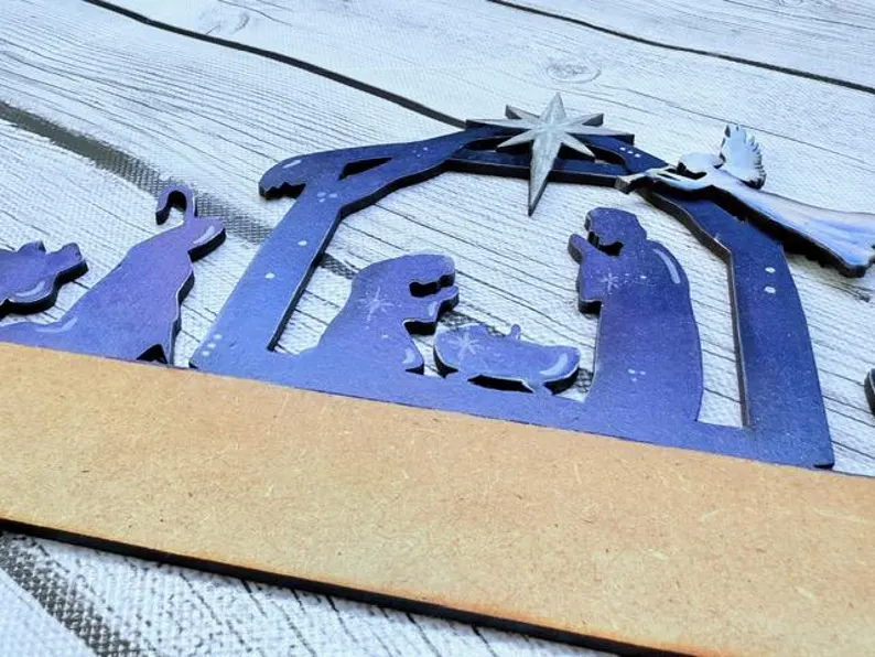 Red Rooster Laser Arts A close-up of the Interchangeable Door Hanger Insert - Nativity Scene shows Mary, Joseph, baby Jesus, an angel, and animals on a light wood base with a blank brown strip—ideal for personalizing your own DIY Christmas decor.
