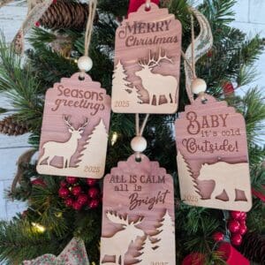 Red Rooster Laser Arts The Holiday Tag Ornament Set – Large Pre-Finished Wooden Christmas Collection (Set of 4) features ornaments labeled 2025, each with animal silhouettes and festive phrases, perfect for decorating a Christmas tree with red berries and pinecones.