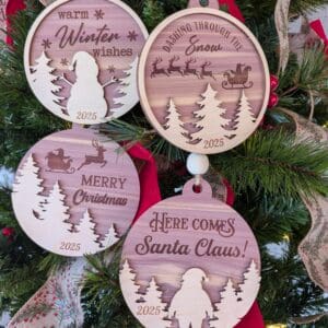Red Rooster Laser Arts Four large Woodland Christmas ornaments from the Pre-Finished Laser-Cut Collection hang on a decorated tree. Each set of 4 features festive 2025 engravings, red ribbons, and greenery in the background.