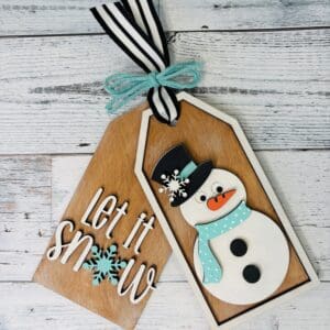 Red Rooster Laser Arts The DIY Ready to Craft boxed Kit - “Let it Snow” includes two wooden gift tags with ribbon and blue twine: one tag reads "Let it snow" with a snowflake, and the other features a festive snowman in a top hat and blue scarf. Perfect for crafting!.