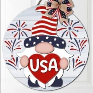 Red Rooster Laser Arts The DIY Door Hanger Kit - "Patriotic USA Gnome" features a round sign with a gnome in a stars-and-stripes hat holding a red heart labeled USA, fireworks background, and an American flag bow at the top.