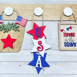 Red Rooster Laser Arts The DIY Interchangeable Wall Peg System Decor - Patriotic Collection includes a wooden base with a basket of American flags, three stars spelling USA, and a "Home of the Brave" sign in festive red, white, and blue accents.