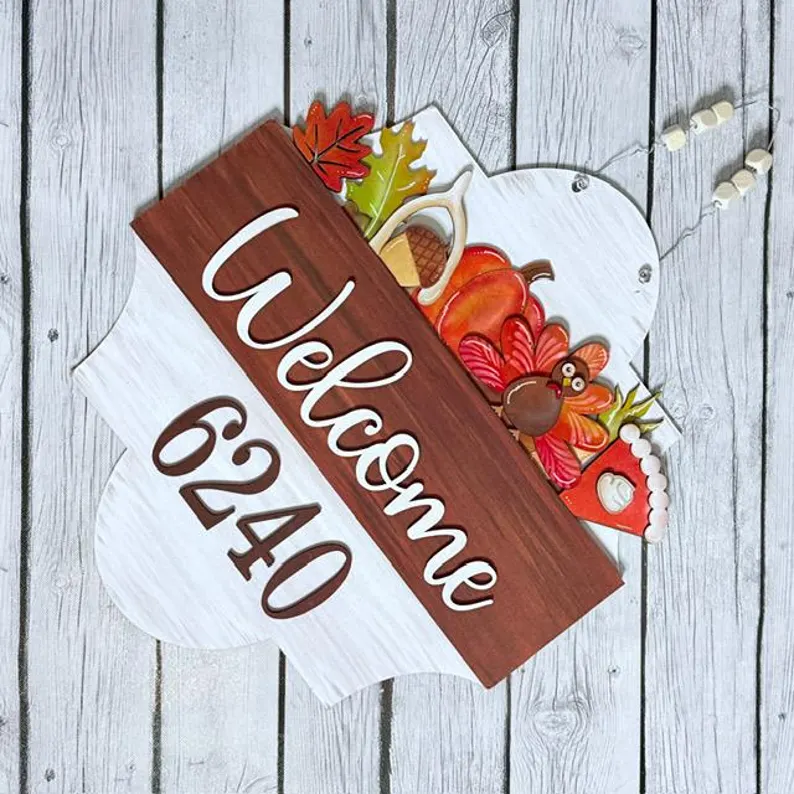 Red Rooster Laser Arts A wooden sign reading "Welcome 6240" features charming fall decorations such as a turkey, leaves, pie, a coffee pot, and beads—all set against a light wooden background. Perfect for the season, this display would pair beautifully with the Interchangeable Door Hanger Insert - Fall Coffee Cups to add even more festive charm to your entryway.