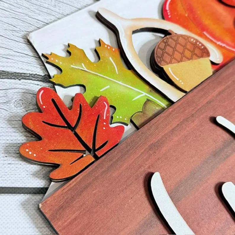 Red Rooster Laser Arts Bring autumn charm to your home with the Interchangeable Door Hanger Insert - Fall Coffee Cups, featuring colorful wooden cutouts of leaves, an acorn, and an antler layered over a wood-textured sign on a white wood background—perfect for your next DIY door hanger project.