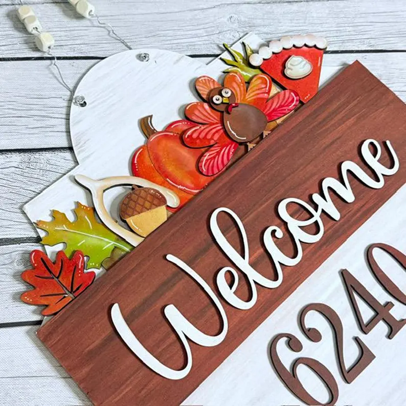 Red Rooster Laser Arts A decorative wooden sign with "Welcome" and festive fall accents—a pumpkin, leaves, an acorn, a slice of pie, and a cartoon turkey on a white wood background—pairs perfectly with the Interchangeable Door Hanger Insert - Fall Coffee Cups for a charming autumn display.