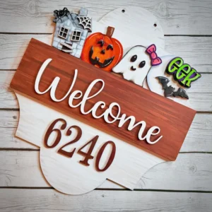 Red Rooster Laser Arts A wooden sign featuring “Welcome 6240” is surrounded by Halloween-themed cookie decorations—a haunted house, pumpkin, ghost, “EEK” sign, and bat—all set against a white wooden background. For seasonal versatility, effortlessly transition your décor after Halloween by swapping in the Interchangeable Door Hanger Insert - Thanksgiving Harvest to celebrate the warmth and gratitude of fall.