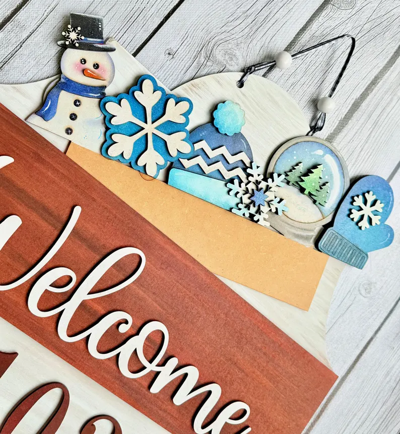 Red Rooster Laser Arts Bring a festive touch to your home with the Interchangeable Door Hanger Insert - Winter Wonderland, a decorative wooden sign showcasing “Welcome” in charming winter style. This piece features blue and white snowflakes, a cheerful snowman, hat, mitten, and snow globe on a gray wood background. Pair it with the DIY Cute Halloween Interchangeable Door Hanger Insert Kit from Red Rooster Laser Arts to keep your seasonal décor fresh and delightful all year long.