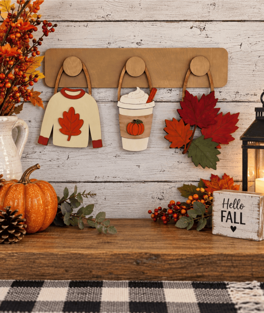 Red Rooster Laser Arts DIY Interchangeable Wall Peg System Decor - Cozy Fall features a charming wooden autumn display with sweaters, pumpkin drinks, leaves, and interchangeable wall hangings. It’s accented by pumpkins, berries, a lantern, candle, Hello Fall sign and other rustic fall elements on a wooden table—perfect for easily updating your decor for patriotic celebrations or any season.