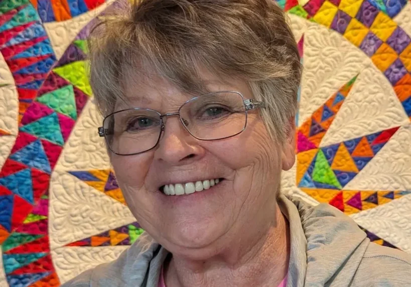 A woman standing in front of a quilt.